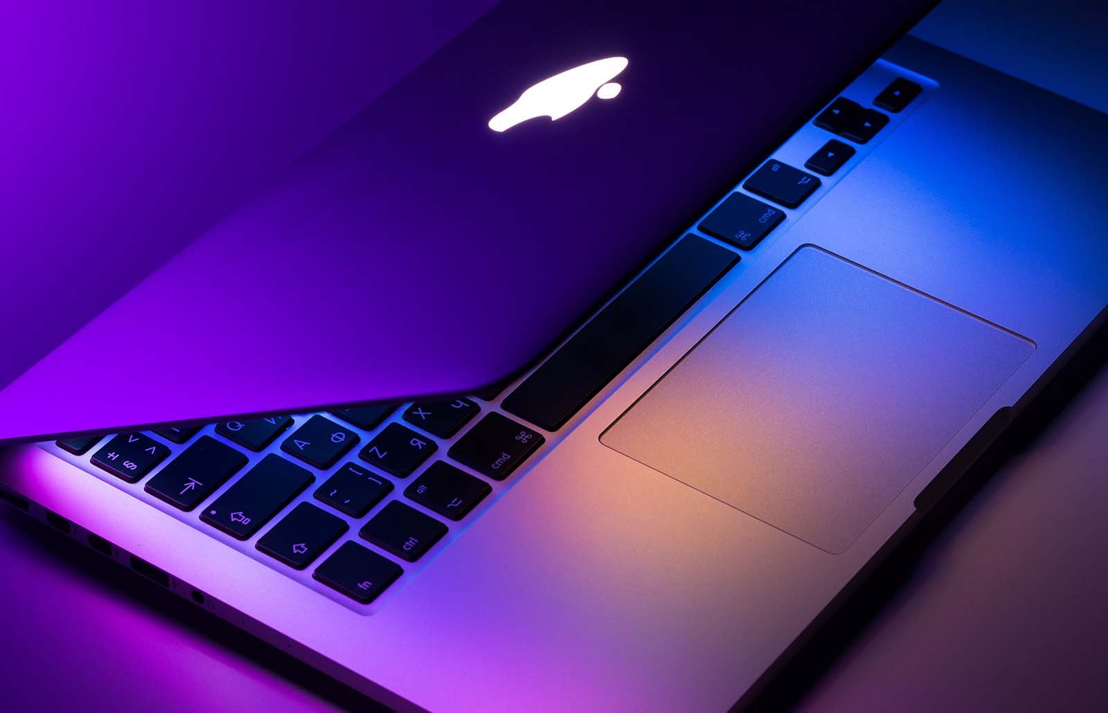 A laptop with a visible logo sits on a surface, surrounded by purple light in an indoor setting.