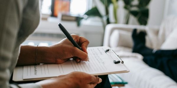 person writing on paper attached to clipboard